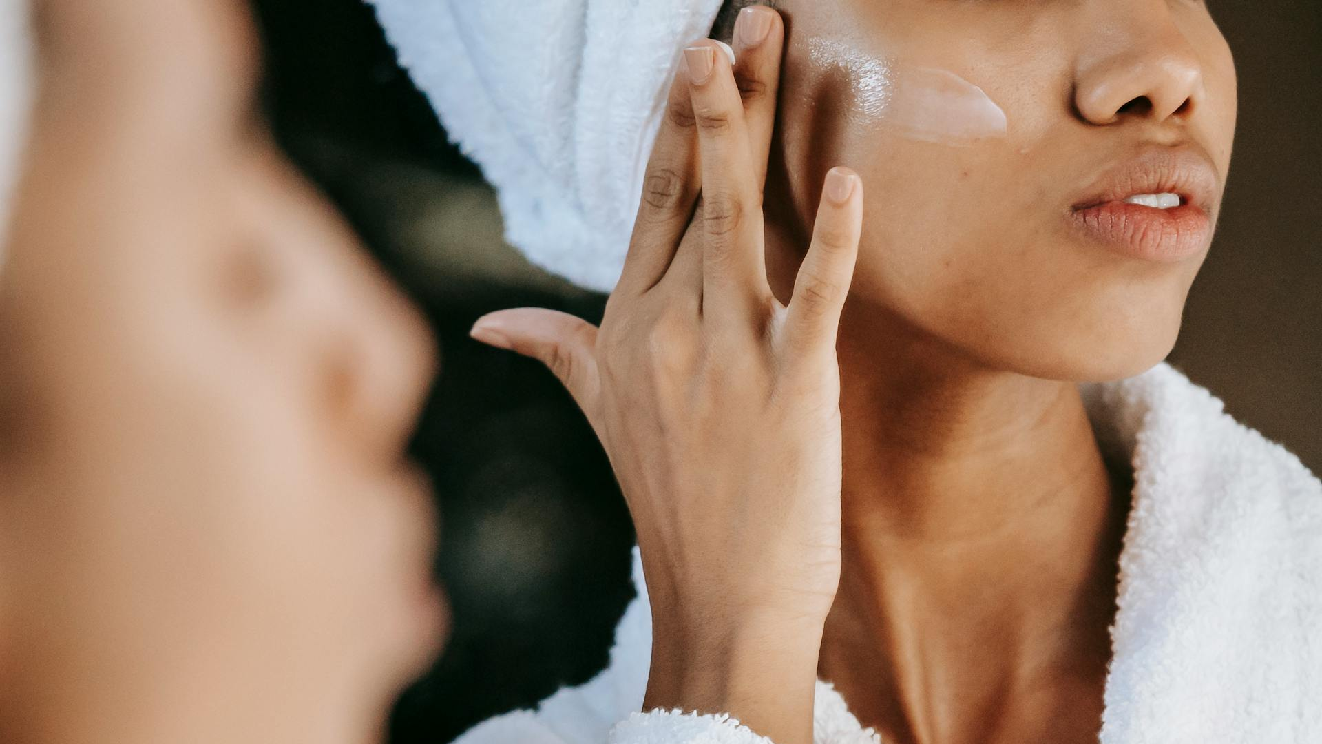 A close-up of a Black woman applying moisturiser to her cheek